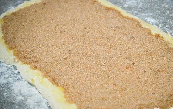 1. Этап. Булочки с корицей и пахтой: 5. Равномерно выложить сахарную начинку по всему тесту, оставляя границы по краям 1 см. Начиная с длинной стороны, свернуть тесто в рулет. Защипнуть края. Выложить швом вниз на рабочую поверхность.