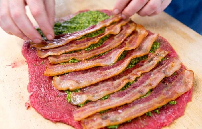 1. Этап. Говяжий рулет: 2. Нарежьте бекон ломтиками и обжарьте его до полуготовности. Выложите отбитое мясо, смажьте его слоем пасты из петрушки (песто), выложите ломтики бекона поперек волокон.