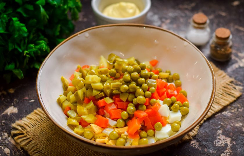 1. Этап. Оливье по-царски: Нарежьте соленые огурцы кубиками, добавьте к остальным ингредиентам, также всыпьте горошек.