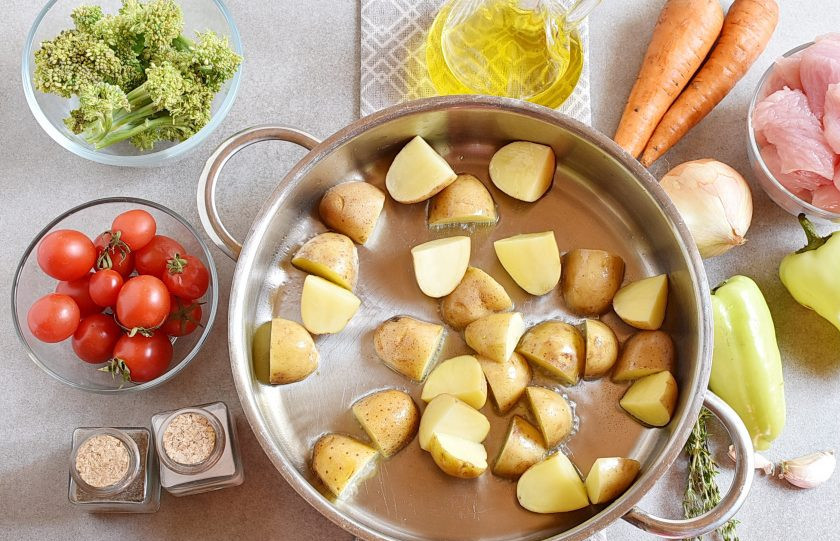 1. Этап. Индейка с овощами на сковороде: Молодой картофель вымойте, обсушите и нарежьте половинками вместе с кожурой. Разогрейте масло в глубоком сотейнике, и обжарьте картофель до легкого румянца.