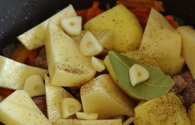 1. Этап. Тушеный картофель со свининой: Выложите картофель к остальным ингредиентам в чашу мультиварки. Добавьте очищенные зубчики чеснока, лаврушку, посолите и поперчите.