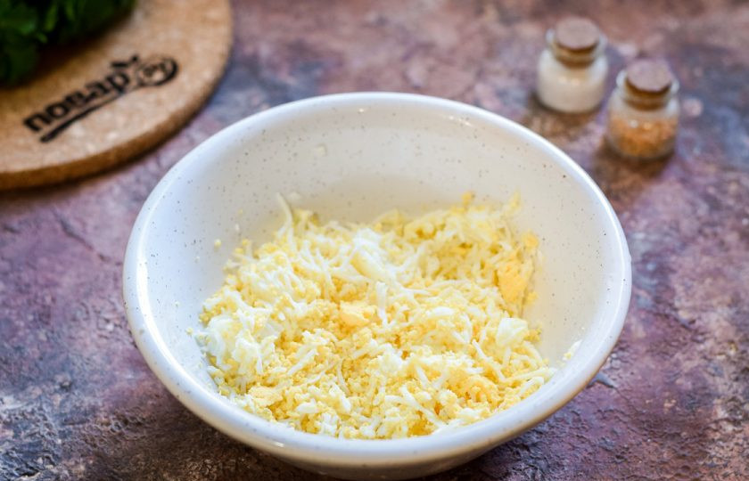 1. Этап. Крабовые палочки Очаровашки: Куриные яйца отварите и почистите, натрите на самой мелкой терке и переложите в миску. Уберите яйца в сторону.