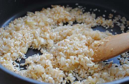 1. Этап. Ризотто с кабачками и помидорами: Далее измельчаем репчатый лук, добавляем на сковороду еще немного масла и жарим на нем лук до золотистого цвета. После этого высыпаем на сковороду рис, жарим его с луком, помешивая, 1-2 минуты.