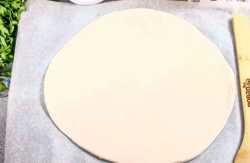1. Этап. Пицца с колбасой из слоеного теста: Слоеное тесто заранее разморозьте, если покупали готовое. Раскатайте его на пергаментной бумаге в округлый пласт.