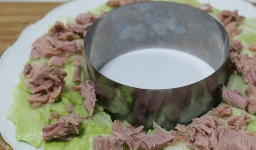 1. Этап. Салат Рождественский венок с тунцом: Подготовить блюдо для подачи. В середине выложить кольцо. Вокруг кольца выложить листья салата. На них отцеженные кусочки тунца.