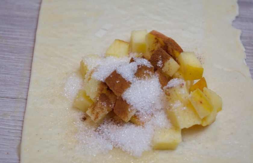 1. Этап. Конвертики из слоеного бездрожжевого теста: Добавьте немного корицы. Соедините края теста, заключив начинку внутри. Получатся так называемые конвертики. Хорошо соедините края. Лучше всего внутренний край квадратов промазать взбитым желтком. Тогда при запекании яблочная карамель не растечется.