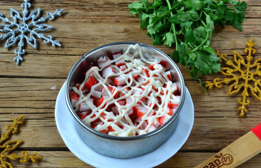 1. Этап. Салат Коррида с крабовыми палочками: Крабовые палочки нарежьте мелким кубиком и выложите следующим слоем, снова покройте майонезом.