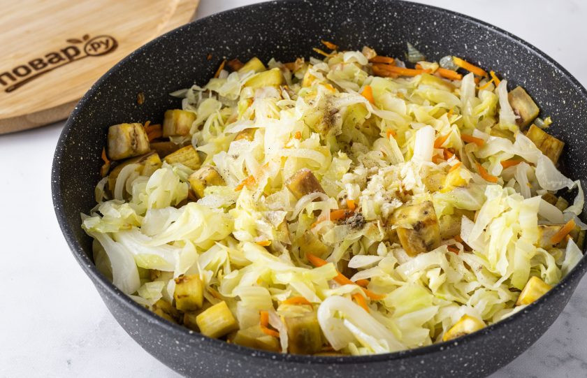 1. Этап. Капуста с баклажанами: После добавьте капусту. Посолите и поперчите. Добавьте измельченный чеснок. Накройте крышкой, тушите на небольшом огне 15-20 минут. Если овощи будут прилипать, то можно добавить еще немного горячей воды.