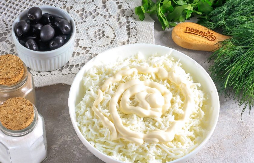 1. Этап. Салат с ананасами на Новый год Кролика 2023: Натрите отварные белки на терке с мелкими ячейками в глубокую емкость и добавьте немного майонеза. Тщательно перемешайте, это будет 