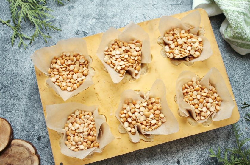 1. Этап. Пирожное Корзиночки с вареной сгущенкой и орехами: Разделите тесто на равные части и выложите по одному в формочки для корзиночек. Пальцами распределите тесто по дну и стенкам толщиной примерно 4-5 миллиметров. Наколите вилкой тесто на дне формочек. Выложите на тесто бумагу для выпечки и заполните корзиночки бобовыми.