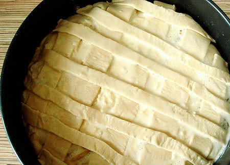 1. Этап. Луковый пирог из слоеного теста: Заливаем яичной смесью начинку. Оставшуюся часть теста раскатываем, режем полосками и укладываем на пирог равномерно. Смазываем пирог желтком.