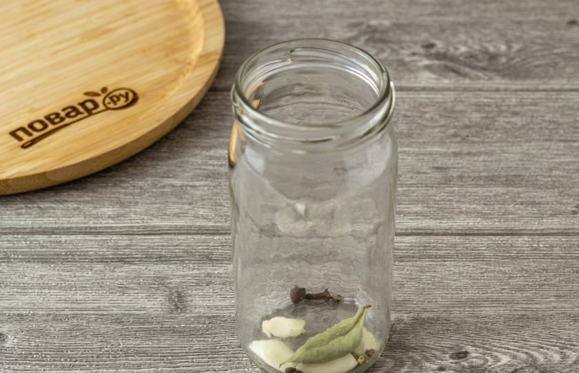 1. Этап. Маринованная морковь на зиму: На дно чистой стерилизованной банки выложите очищенный разрезанный чеснок, все специи и лавровый лист.