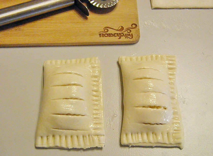 1. Этап. Слойки с творогом из готового слоеного теста: Закройте слойки тестом, край закрепите вилочкой, как в чебуреках. Смажьте белком с помощью силиконовой кисточки.