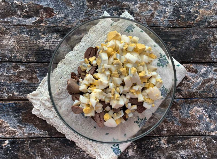 1. Этап. Салат с куриными сердечками и печенью: Яйца очистите от скорлупы, мелко нарежьте и выложите в тарелку.