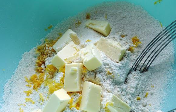 1. Этап. Булочки с малиной и лимонной глазурью: 1. Разогреть духовку до 200 градусов. Выстелить противень пергаментом. Натереть цедру лимона. Чтобы приготовить тесто для булочек, просеять вместе все сухие ингредиенты и смешать с цедрой одного лимона. С помощью вилки добавить масло в муку и перемешать, пока смесь не будет напоминать мокрый песок.