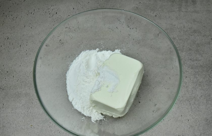 1. Этап. Торт Медок: В миске соедините ванилин, сахарную пудру и творожный сыр. Взбейте крем миксером до пышности и однородности.