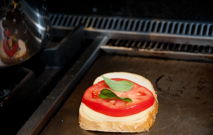 1. Этап. Горячий бутерброд на сковороде: 3. На сковороду выложите кусочек белого хлеба. На хлеб положите кусочек сыра Проволони (если вы его нашли и используете), затем кружок помидора и пару листиков базилика.