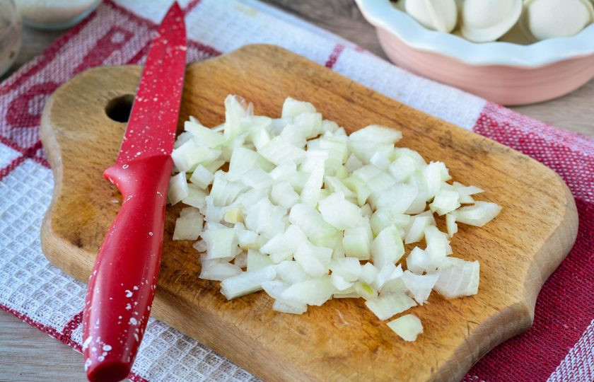 1. Этап. Пельмени тушеные с морковью и луком: Нарежьте кубиками очищенный репчатый лук.