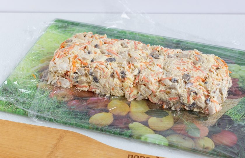 1. Этап. Салат Новогодний подарочек: Досочку застелите пищевой пленкой, выложите на неё салат и сформируйте прямоугольник. Оберните салат пищевой пленкой и уберите в морозильную камеру на 30 минут.