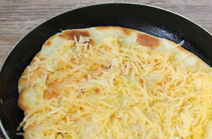 1. Этап. Домашняя пицца на тонком тесте: Обжаривайте на сковороде тесто с обеих сторон на среднем огне по пять минут. Оно должно стать румяным. Натрите на терке твердый сыр и выложите половину на заготовку для пиццы.
