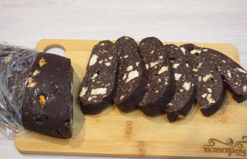 1. Этап. Шоколадная колбаса: Переложите теперь шоколадную колбасу на что-то плоское и ровное. Поместите в морозилку на 30-40 минут. Колбаска застынет. Достаньте колбаску. Удалите с неё пленку, нарежьте колбасу острым широким ножом на кусочки.
