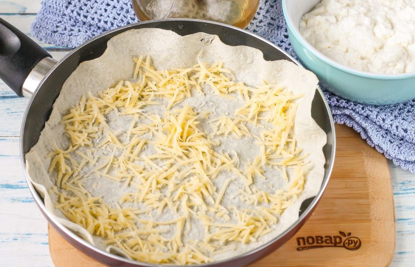1. Этап. Пирог из лаваша на сковороде: Натрите твердый сыр на терке с мелкими ячейками и присыпьте первый слой.