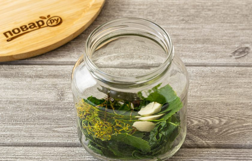 1. Этап. Маринованные огурцы с уксусом: В чистую стерилизованную банку выложите зонтик укропа, лист смородины и лист хрена. Добавьте душистый перец, лавровый лист и очищенный зубчик чеснока.