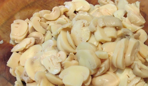 1. Этап. Салат из курицы с фасолью: Откройте банку с шампиньонами и слейте маринад. Грибочки нарежьте пластинками. Вместо шампиньонов можно использовать любые маринованные грибы (к примеру, опята).