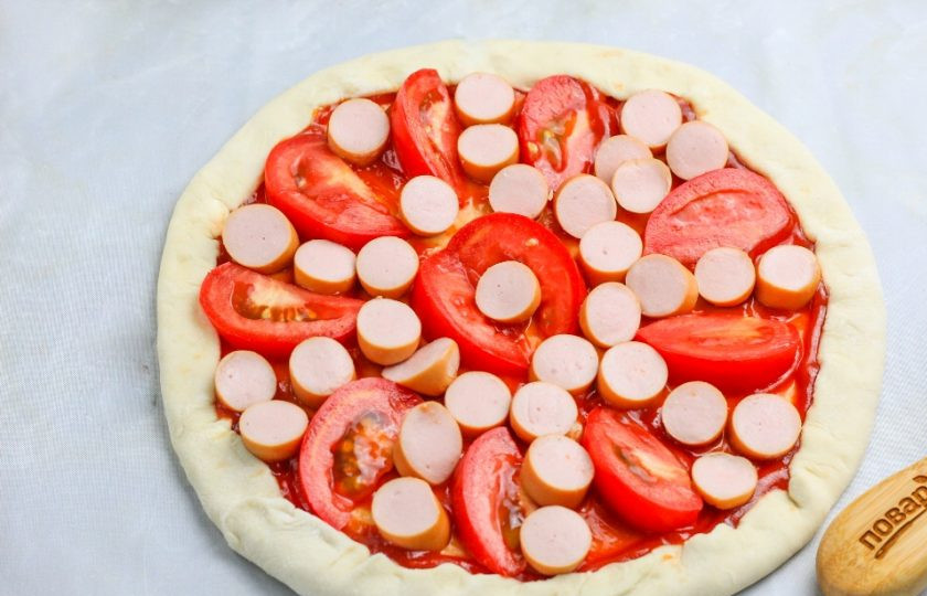 1. Этап. Быстрая пицца: Выложите ломтики помидоров и нарезку сосисок. Можно добавить маслины, оливки или нарезанный лук. Разогрейте духовку до 220 градусов.