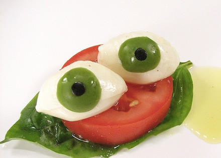 1. Этап. Салат Капрезе на Хэллоуин: 5. Сделайте столько глаз (по паре!), сколько вам нужно. На дольку помидора - два глаза.В тарелку выложите лист базилика, на него - кружок помидора, затем разрезанный наполовину кружок Моцареллы (две половинки) и сверху - 