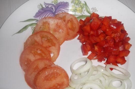 1. Этап. Куриная грудка под шубой в духовке: Пока займитесь овощами. Лук почистите и нарежьте колечками. Помидор помойте и нарежьте кружками, а перец — мелкими кубиками.