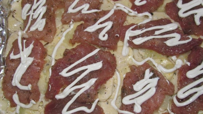 1. Этап. Картошка, запеченная со свининой и сыром: Свинину нарезаем порционными кусочками, слегка отбиваем и выкладываем на противень. Солим и перчим, поливаем майонезом.