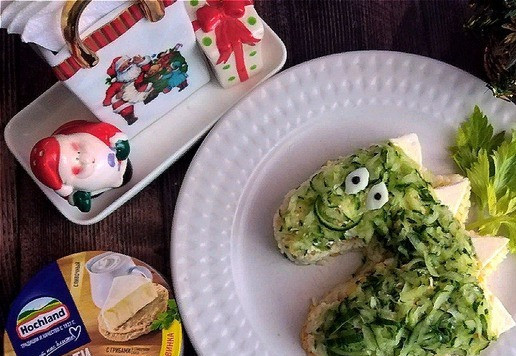 1. Этап. Салат Новогодний Дракончик: И пятый слой (самый верхний) - натёртый огурец на тёрке средней величины. Прежде чем слой выкладывать, с натёртого огурца нужно отжать сок. Аккуратно распределяем по всей поверхности. Ничего не спадёт, тк приклеится к майонезной сетке. Дракончик готов. Теперь из оставленного кусочка яичного белка кухонными ножницами вырезаем глазки. Ножом протыкаем по центру и вставляем по горошине чёрного перца. Из шкурки огурца вырезаем улыбающийся ротик и коготки. Помещаем так, чтобы мордочка была миловидная и добрая. Крылышки у меня будут из листьев черешкового сельдерея. Они крупные и будут здесь в тему.