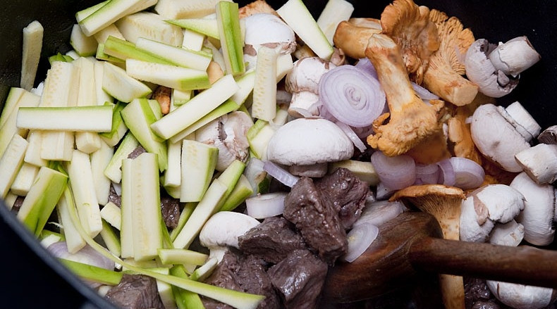 1. Этап. Мясной пирог под слоеным тестом: В сковороде разогреваем оливковое масло, обжариваем в нем кусочки мяса до румяной корочки со всех сторон. Затем добавляем все остальные нарезанные ингредиенты и готовим, помешивая, на среднем огне 3-4 минуты.