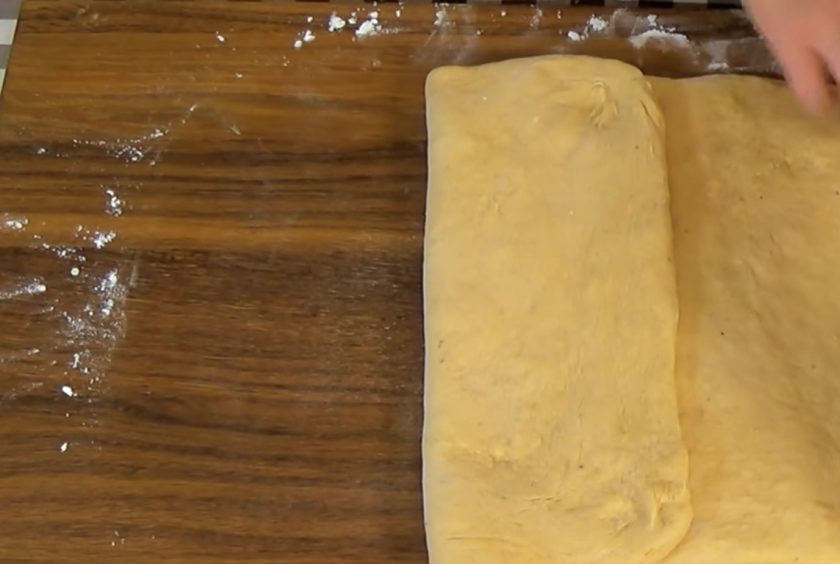 1. Этап. Булочки с тыквой и корицей: 3. Постепенно добавьте просеянную муку и замесите мягкое тесто в течение 10 минут. Накройте миску пленкой и оставьте в теплом месте, чтобы тесто увеличилось вдвое. На посыпанной мукой доске сформируйте из теста прямоугольник.