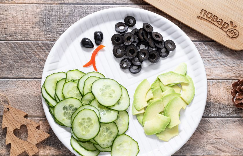 1. Этап. Вегетарианский салат Змея: Огурец нарежьте очень тонкими кружочками (можно на специальной терке), подсолите и оставьте на 10-15 минут, чтобы он выделил сок. После промойте в холодной воде и обсушите каждый кружочек с помощью бумажных салфеток. Так огурец будет пластичным и гибким. На очень тонкие ломтики нарежьте авокадо. Маслины порежьте кружочками, а из одной вырежьте глаза для змеи. Из кусочка красного болгарского перца вырежьте язык.