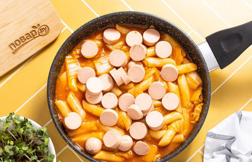 1. Этап. Рисовые токпокки: Сосиски очистите от оболочки, нарежьте кружочками. Добавьте в сковороду. Прогрейте все вместе еще 1-2 минуты.