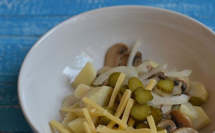 1. Этап. Салат с грибами и картофелем: Выложите обжаренные грибы и отварной картофель в миску, добавьте к нему нарезанный репчатый лук, корнишоны и твердый сыр. Посолите и поперчите салат.