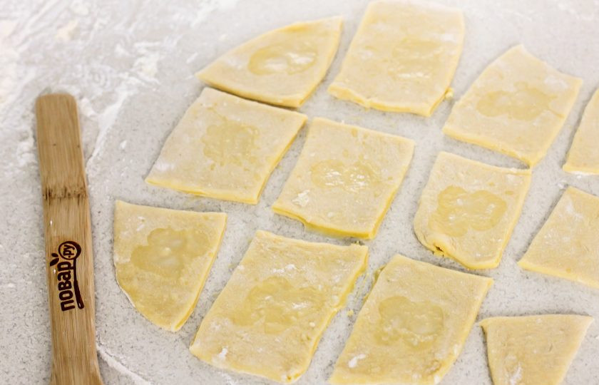 1. Этап. Хворост Розочки: Разделите тесто на 2-3 части и раскатайте каждую из них в округлый или прямоугольный пласт, подпыляя рабочую поверхность мукой. Нарежьте пласт квадратиками или прямоугольниками. Желательно, чтобы нижние квадраты были крупнее, а верхние — мельче. Можно оставить квадраты целыми, а можно на их краях сделать надсечки, чтобы розочки получились более пышными.