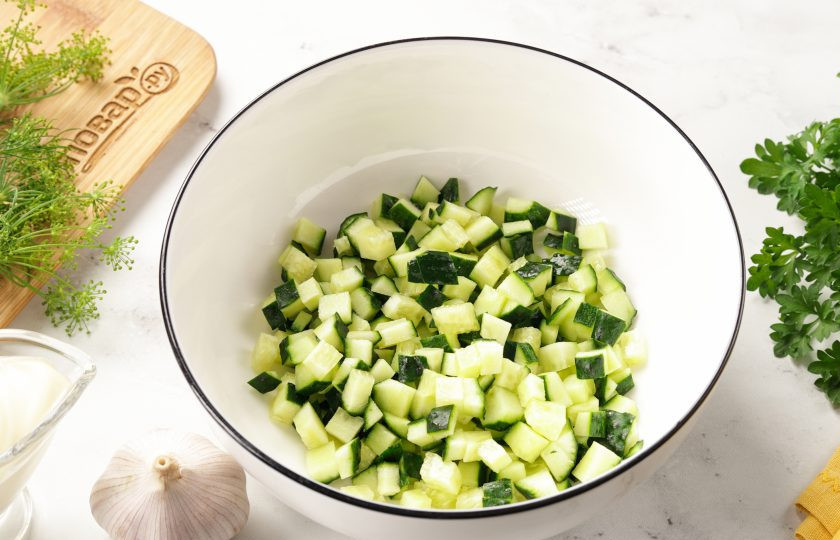 1. Этап. Салат с яйцом, сыром, кукурузой и огурцом: Огурцы нарежьте кубиками и переложите в глубокую миску или сразу в салатник.