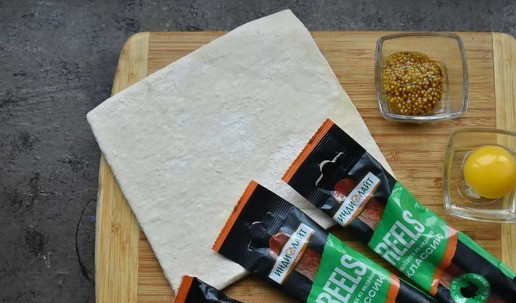 1. Этап. Колбаски Рилс в тесте: Для приготовления потребуется три колбаски Reels классик, любая горчица на ваш вкус, один лист слоеного бездрожжевого теста. яичный желток и любая зерновая смесь.