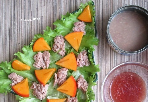 1. Этап. Новогодний салат Тунец и хурма: На листья салата разложите филе тунца, слегка отжимая от жидкости. Хурму разрежьте на 4 части, затем нарежьте дольками, выложите на салат.