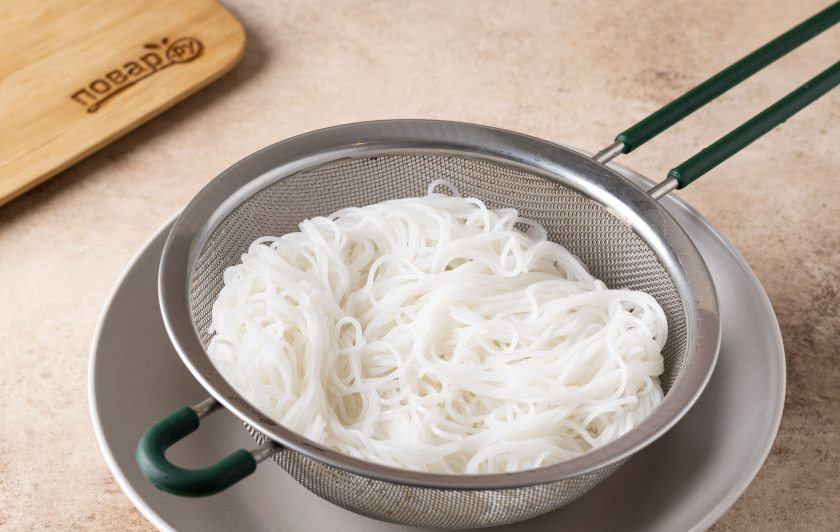 1. Этап. Тайское блюдо из рисовой лапши: Рисовую лапшу замочите в горячей воде на полчаса, чтобы она стала пластичной и мягкой. Затем промойте в холодной воде и откиньте на сито, немного обсушите.