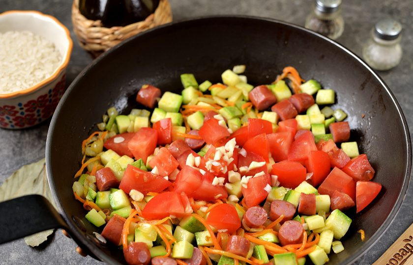 1. Этап. Рис с колбасками и овощами: Вырежьте место плодоножки на помидорах, нарежьте их кубиком, измельчите чеснок, добавьте в сковороду, тушите еще несколько минут.