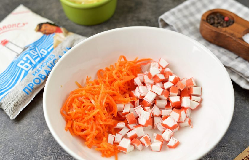 1. Этап. Салат из крабовых палочек, моркови по-корейски и сыра: Почистите крабовые палочки от целлофана, нарежьте мелким кубиком, выложите в глубокую миску. Морковь по-корейски тоже измельчите ножом, так ее будет удобнее есть в готовом салате.