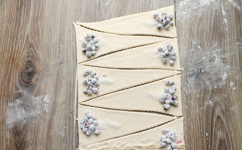 1. Этап. Круассаны с черникой: Чернику переберите и обваляйте в крахмале. На широкий край каждого треугольника насыпьте немного сахара и разложите чернику.