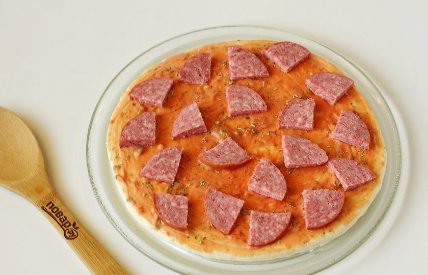 1. Этап. Пицца на готовой основе в микроволновке: Колбасу нарежьте произвольно и распределите по всей основе.