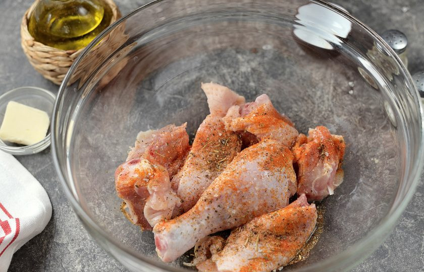 1. Этап. Батат с курицей в духовке: Нарежьте окорок крупными кусками, выложите в глубокую миску, всыпьте приправу и ароматные сушеные травы, влейте масло.