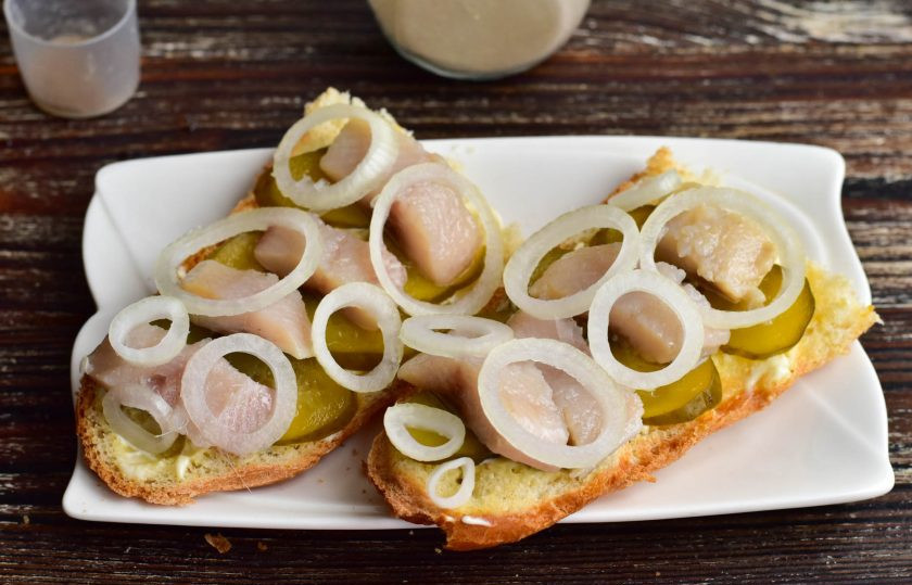 1. Этап. Голландские бутерброды с селедкой на багете: На рыбу выложите репчатый лук, который нарежьте кольцами.