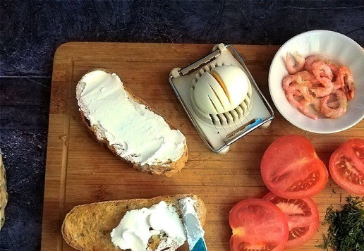 1. Этап. Бутерброды с творожным сыром и креветками: Креветки нужно почистить. Хлеб подсушите любым способом. Я это сделаю в тостере. Намазываем ломти подсушенного хлеба щедро сыром ТМ HOCHLAND крем-чиз в кондитерском мешке. Яйцо я разрежу на дольки специальным приспособлением. Режьте так, как вам удобно, чтобы дольки были поперечные. У меня получилось 6 долек. Помидор нарезаем тоже дольками плоскими. Я возьму для бутербродов 2 дольки. Остатки пойдут для подачи. Укроп мелко рубим.